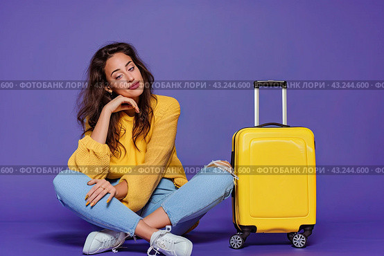 A thoughtful traveler girl sitting next to her luggage on a uniform lilac background. Copy space. The concept of vacation. Стоковое AI-изображение, AI-художник Ярославский Максим / Фотобанк Лори