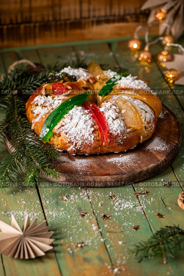 A traditional holiday sweet bread dusted with powdered sugar and adorned with candied fruits and green citrus peel, served on a rustic wooden board with pine branches. Стоковое фото, агентство Ingram Publishing / Фотобанк Лори