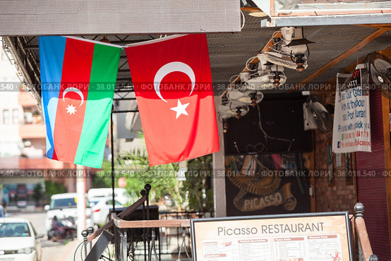 A typical street cafe with flags and menu board is on one of the main streets of the city Alanya, Turkey (2020 год). Редакционное фото, фотограф Кекяляйнен Андрей / Фотобанк Лори