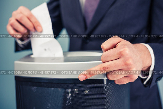 A white collar criminal is displaying obscene gesture while destroying evidence in shredder. Стоковое фото, агентство Ingram Publishing / Фотобанк Лори