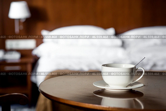 A white cup of hot tea or coffee on a wooden table in the interior of a hotel room. The concept of drinks and comfortable hotel accommodation. Стоковое фото, фотограф Photojuli / Фотобанк Лори