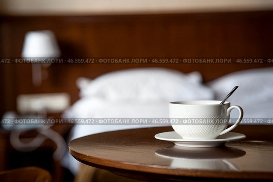 A white cup of hot tea or coffee on a wooden table in the interior of a hotel room. The concept of drinks and comfortable hotel accommodation. Стоковое фото, фотограф Photojuli / Фотобанк Лори