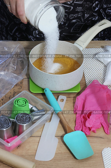 A woman adds sugar to apple juice in a saucepan. She is preparing syrup for homemade marshmallows. Zefir-making tools are nearby on the table. Стоковое фото, фотограф Vadzim Yakubovich / Фотобанк Лори