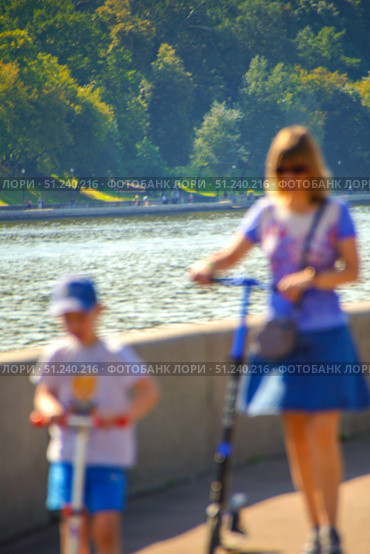 A woman and a child are riding scooters on a sidewalk near a river.  Russia. Moscow. 24.08.25. Редакционное фото, фотограф Ярославский Максим / Фотобанк Лори