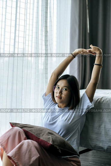 A woman in a white shirt sitting on the bed and raising both arms. Стоковое фото, агентство Ingram Publishing / Фотобанк Лори