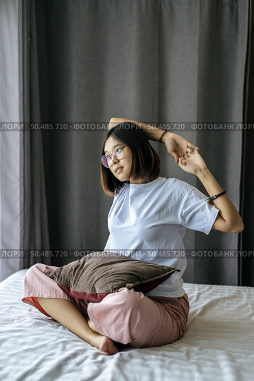 A woman in a white shirt sitting on the bed and raising both arms. Стоковое фото, агентство Ingram Publishing / Фотобанк Лори