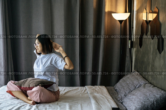 A woman in a white shirt sitting on the bed and raising both arms. Стоковое фото, агентство Ingram Publishing / Фотобанк Лори