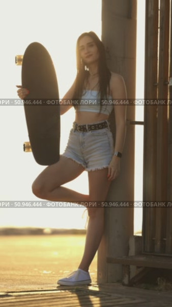 A woman is holding a skateboard and standing in front of a fence. Стоковое видео, видеограф Константин Шишкин / Фотобанк Лори