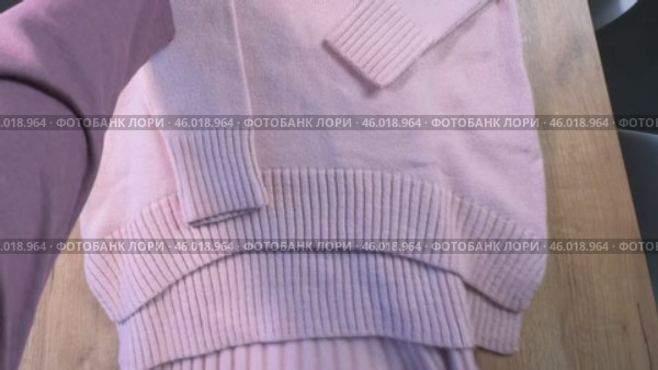 A woman is reviewing a knitted set. A knitted sweater and skirt. She is laying out the clothes on the table. High-Angle Shot. Стоковое видео, видеограф Vadzim Yakubovich / Фотобанк Лори