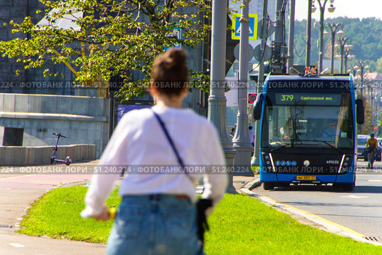 A woman is riding a scooter on a sidewalk next to a blue bus.  Russia. Moscow. 24.08.25. Редакционное фото, фотограф Ярославский Максим / Фотобанк Лори