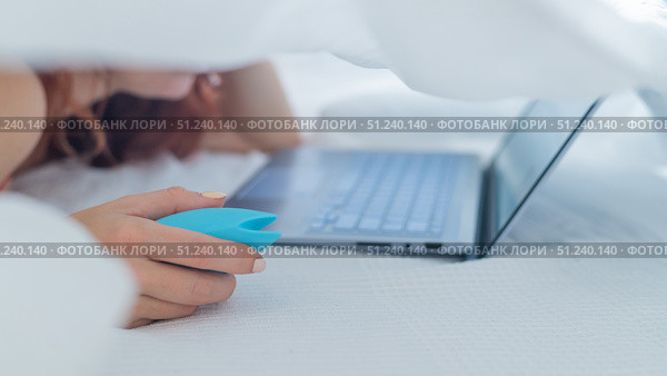 A woman lies in bed holding a clitoral vibrator and watching porn on a laptop. The girl has sex online. Стоковое фото, фотограф Михаил Решетников / Фотобанк Лори