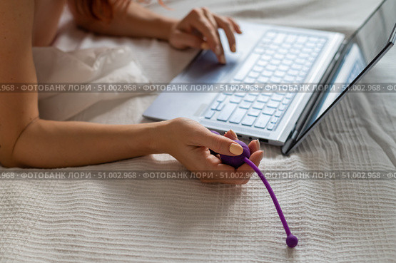 A woman lies in bed holding a vibrator and watching porn on a laptop. Стоковое фото, фотограф Михаил Решетников / Фотобанк Лори