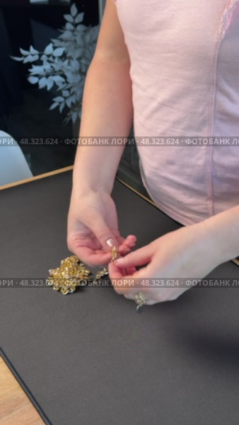 A woman reviewing jewelry, laying out a gold-colored necklace, bracelet, earrings, and ring on a table. Vertical video. Oblique Angle. Стоковое видео, видеограф Vadzim Yakubovich / Фотобанк Лори