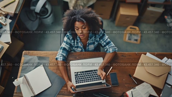 A woman works on her laptop in a cluttered home office. She is focused on her work and surrounded by papers and other work-related items. Стоковое AI-видео, аниматор Данила Большаков / Фотобанк Лори