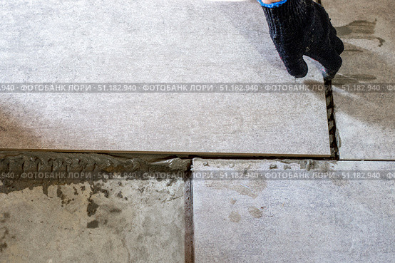 A worker lays gray ceramic tiles during a floor renovation, ensuring precise alignment with plastic spacers. Стоковое фото, фотограф Коханова Наталья / Фотобанк Лори