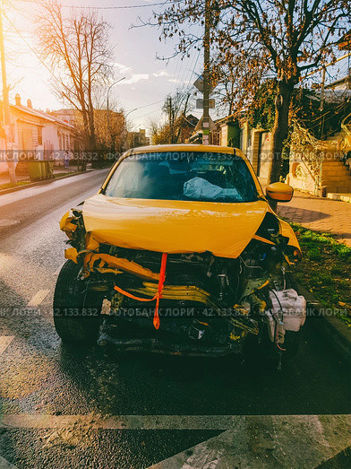 A yellow car wrecked in a car accident stands on a city street on a sunny autumn morning front view. Стоковое фото, фотограф Андрей С / Фотобанк Лори