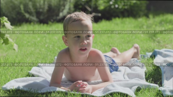 A Young Boy is Relaxing on His Towel in the Bright, Sunlit Grass of a Beautiful Day. Стоковое видео, видеограф Olesia Kondrateva / Фотобанк Лори