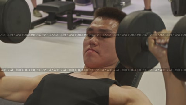 A young man in a black T-shirt is lifting weights in the gym, sweating from the effort. Стоковое видео, видеограф Strunov David / Фотобанк Лори