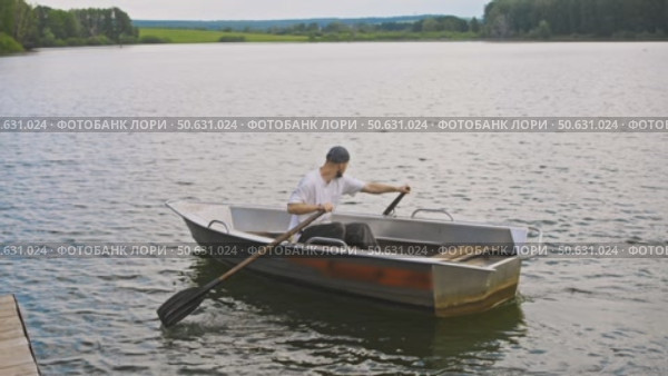 A young man is paddling a boat next to a pier in the middle of the river in summer. Стоковое видео, видеограф Strunov David / Фотобанк Лори
