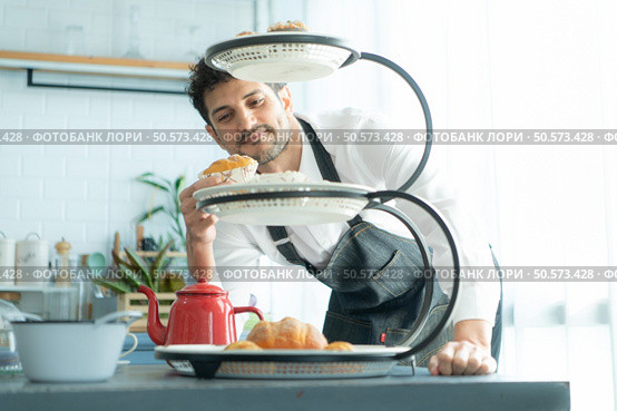 A young man puts on an apron to make dessert to eat with his wife. Checking the completeness of the finished dessert. Стоковое фото, агентство Ingram Publishing / Фотобанк Лори