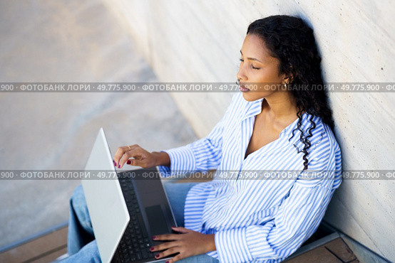 A young woman sits against a wall outdoors, focused on her laptop, embodying modern worklife balance. The tranquil setting boosts her creativity and productivity, enabling her to thrive. A Focused Young Woman is Quite Intently Working on Her Laptop While Enjoying the Outdoors. Стоковое фото, агентство Ingram Publishing / Фотобанк Лори