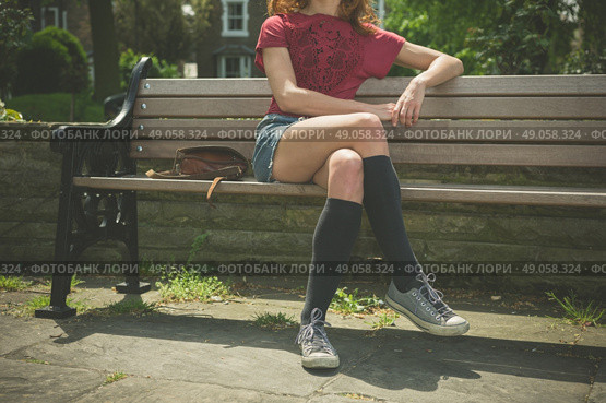 A young woman wearing knee high socks is sitting on a park bench. Стоковое фото, агентство Ingram Publishing / Фотобанк Лори
