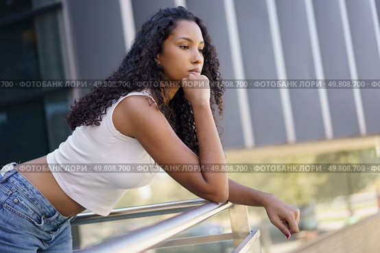 A young woman with beautiful, curly hair leans thoughtfully against a railing in a bustling city, embodying a sense of introspection and tranquility amid the vibrant urban life that surrounds her. A thoughtful young woman is peacefully leaning on a railing while outdoors in nature, Стоковое фото, агентство Ingram Publishing / Фотобанк Лори
