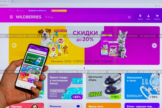 Adygea, Russia - August 09, 2023: hand man with smartphone making purchases in Wildberries online store in mobile application against background Wildberries marketplace web page open computer monitor. Редакционное фото, фотограф Андрей С / Фотобанк Лори