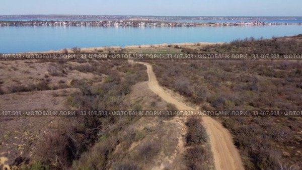 Aerial view, flying over a dirt road in steppe, in the background the pond and village. Camera moving forwards above steppe to the pond side. Khadzhibey Estuary, Odessa region, Ukraine. Стоковое видео, видеограф Некрасов Андрей / Фотобанк Лори
