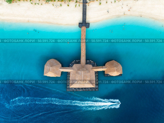 Aerial view of bungalow, boat in blue sea at sunset in summer. Restaurant on the ocean. Top drone view of wooden hotel, azure water, white sandy beach, palm trees. Luxury resort in Kendwa, Zanzibar. Стоковое фото, агентство Ingram Publishing / Фотобанк Лори