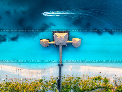 Aerial view of bungalow, boat in Indian Ocean at sunset in summer. Restaurant on the sea. Top drone view of wooden hotel, azure water, white sandy beach, palm trees. Luxury resort in Kendwa, Zanzibar. Стоковое фото, агентство Ingram Publishing / Фотобанк Лори