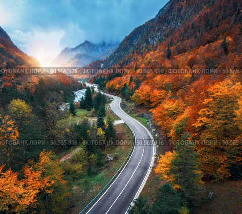 Aerial view of curvy road and orange forest in mountains at sunset. Golden autumn in Italy. Top view of winding road, colorful red trees, river, mountains in fall. Empty road, woods. Moody landscape. Aerial view of curvy road and orange forest in mountains in fall. Стоковое фото, агентство Ingram Publishing / Фотобанк Лори
