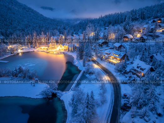 Aerial view of fairy alpine village in snow, road, forest, Jasna lake, houses, street lights at winter night. Top view of mountains, illumination, snowy pine trees at twilight. Kranjska Gora, Slovenia. Стоковое фото, агентство Ingram Publishing / Фотобанк Лори