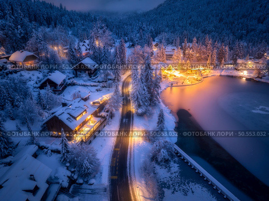 Aerial view of fairy town in snow, road, forest, Jasna lake and houses with lights at night in winter. Top view of mountain village, illumination, snowy pine trees at dusk in Kranjska Gora, Slovenia. Стоковое фото, агентство Ingram Publishing / Фотобанк Лори