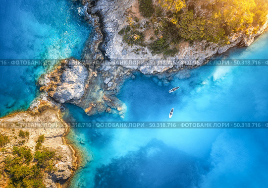 Aerial view of floating board and people on blue sea, rocks with trees at sunset in summer in Blue lagoon, Oludeniz, Turkey. Tropical landscape. Kayaks on clear water. Active travel. Top view of canoe. Стоковое фото, агентство Ingram Publishing / Фотобанк Лори