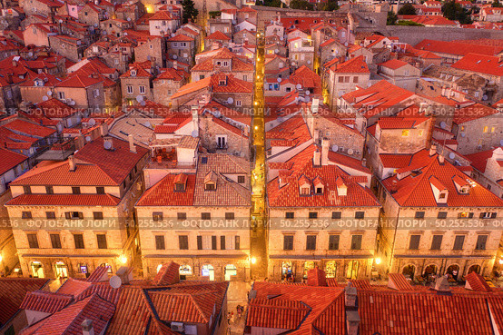 Aerial view of houses with red roofs at night in Dubrovnik, Croatia. Top view of beautiful architecture in old city. City lights, historical centre, buildings, walking people in illuminated streets. Стоковое фото, агентство Ingram Publishing / Фотобанк Лори