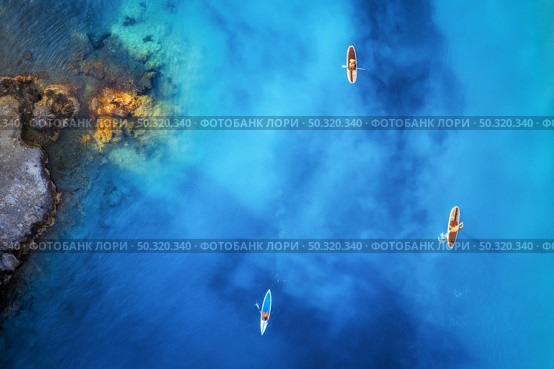 Aerial view of people on floating sup boards on blue sea, rocks, stones at sunset in summer in Oludeniz, Turkey. Tropical landscape. Kayaks on clear water. Active travel. Top view of canoe. Sport. Стоковое фото, агентство Ingram Publishing / Фотобанк Лори