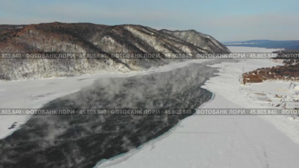 Aerial view of the ice-free source of the Angara River near Lake Baikal, surrounded by snow-capped hills. Mist and steam rise from the water. Стоковое видео, видеограф Виктория Тельминова / Фотобанк Лори