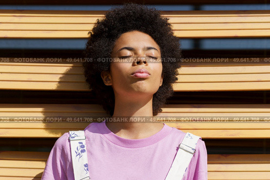 African-American woman getting sunlight on her face with her eyes closed, lost in thought, on a shutter of a modern building.. African-American woman getting sunlight on her face with her eyes closed. Стоковое фото, агентство Ingram Publishing / Фотобанк Лори