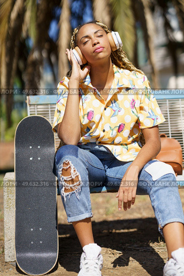 African woman with skateboard. Black girl relaxing after riding skateboard listening to the music outdoors.. African girl with skateboard relaxing after riding skateboard listening to the music. Стоковое фото, агентство Ingram Publishing / Фотобанк Лори