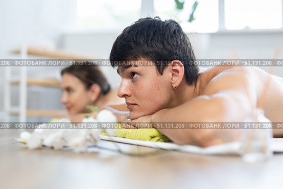 After massage, guy lies on white blanket on floor. Blurry unrecognizable clients girl in background. Стоковое фото, фотограф Яков Филимонов / Фотобанк Лори