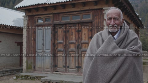 Aged local wearing traditional attire posing near weathered wooden dwelling in isolated mountain settlement, embodying rural heritage. Стоковое AI-видео, аниматор Данил Руденко / Фотобанк Лори