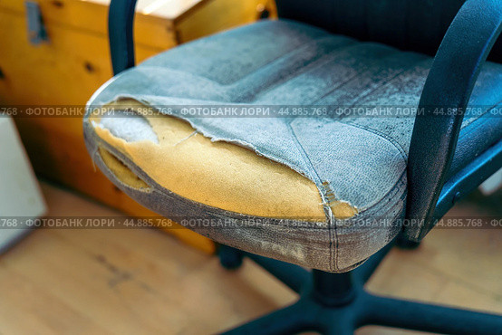 Aging office chair bears the scars of time, with its frayed covering exposing the soft foam beneath. This image speaks to the weariness of work life and the stories held in forgotten furniture. Стоковое фото, фотограф Татьяна Степанищева / Фотобанк Лори