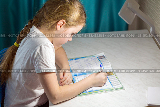An adorable little schoolgirl sits at a desk and does homework in her room. Стоковое фото, фотограф Акиньшин Владимир / Фотобанк Лори