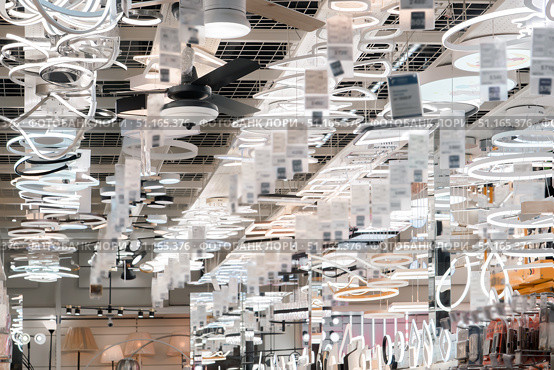 An array of stylish lighting fixtures hangs elegantly from the ceiling of a modern shop. Different types of lamps, sconces, and chandeliers are showcased, highlighting innovative designs. Стоковое фото, фотограф Владимир Разгуляев / Фотобанк Лори