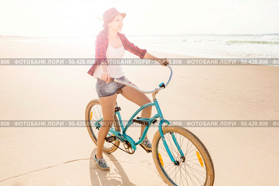 An attractive young woman riding her bicycle on the beach. Стоковое фото, агентство Ingram Publishing / Фотобанк Лори