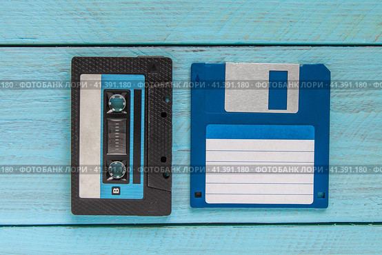 An audio cassette in a black plastic case and a blue floppy disk lie on a blue wooden background. Стоковое фото, фотограф Воловодов Владимир / Фотобанк Лори