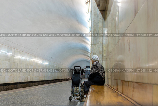 An elderly woman on the bench is waiting for a train at the metro station. (2019 год). Редакционное фото, фотограф Андрей Никитин / Фотобанк Лори