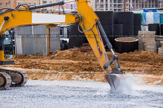 An excavator on a construction site in close-up. The excavator rams the crushed stone with a bucket for construction. Heavy machinery for construction and landscaping. Стоковое фото, фотограф Photojuli / Фотобанк Лори