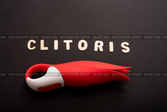 An overhead view of a red tulip shaped clitoral vibrator and the inscription clitoris on a black background. Стоковое фото, фотограф Михаил Решетников / Фотобанк Лори